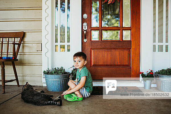 Young boy sitting outside front door with pet cat
