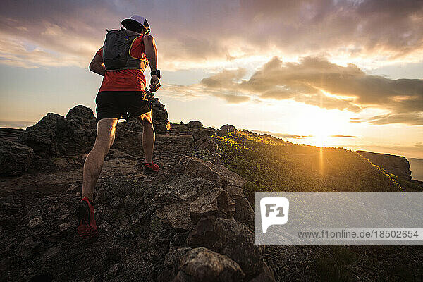 Trail running man running at sunrise with cairn from low angle