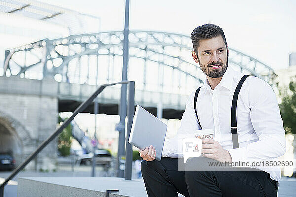 Businessman sitting on the stairs and holding digital tablet with coffee  Munich  Bavaria  Germany