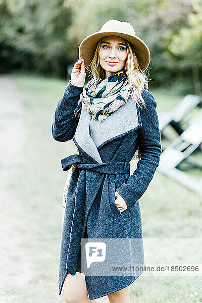 Happy young woman wearing coat and hat with scarf in park