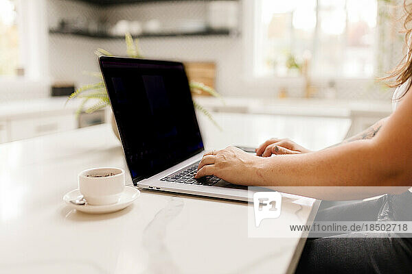 Side view of a woman working on computer with coffee inside
