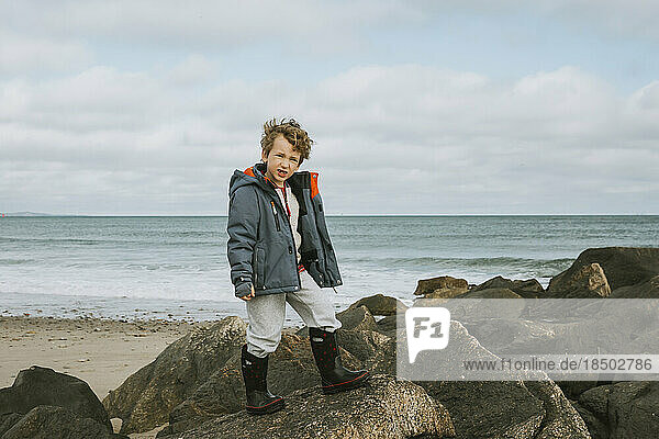 Boy standing on rocks at beach against cloudy sky