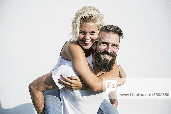 Happy woman enjoying piggyback ride on her boyfriend in front of wall  Bavaria  Germany