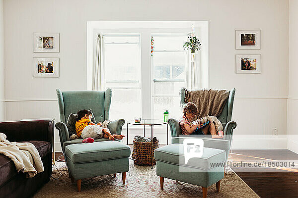 Young boy and girl resting in living room using tablets