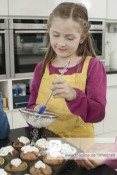 Schoolgirl sprinkle powdered sugar on muffins in home economics class  Bavaria  Germany