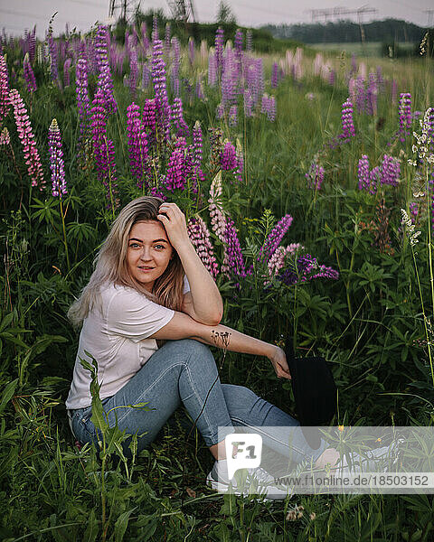 Girl is sitting on a summer field with lupins