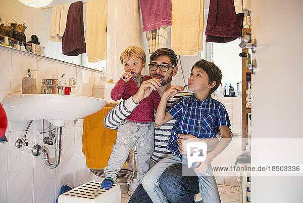 Father and his sons brushing their teeth in bathroom  Munich  Germany