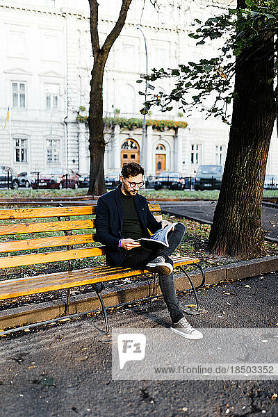 Stylish curly man reading a book while sitting in the park