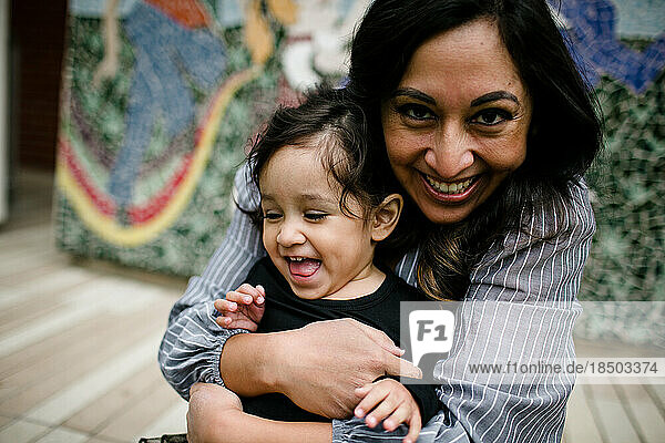 Mother hugging daughter & laughing in front of mural