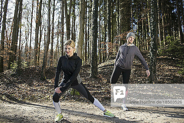 Man and woman doing stretching on fitness trail in nature