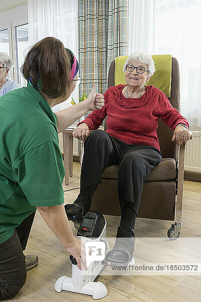 Nurse with senior woman exercising on exercise bike in rest home