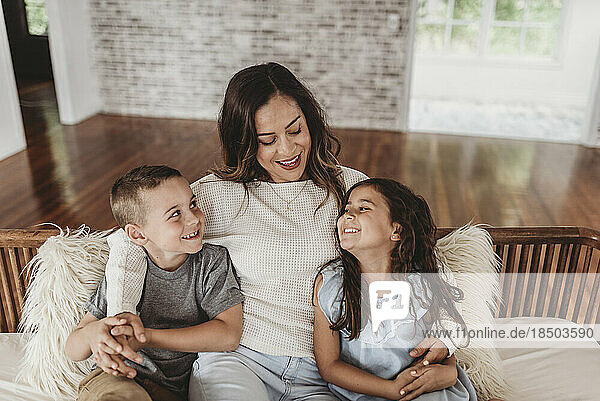 Mother and children smiling at each other while sitting on couch