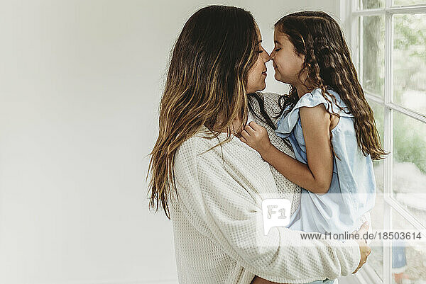 Mother and daughter touching noses in natural light studio