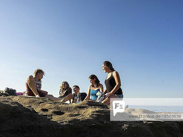 Group of young friends picnicking on rocky beach at Playa de Azkorri  Getxo  Basque Country  Spain