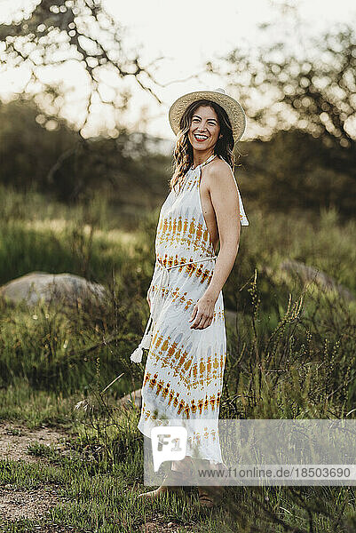Full length portrait of young woman smiling in dress in backlit field