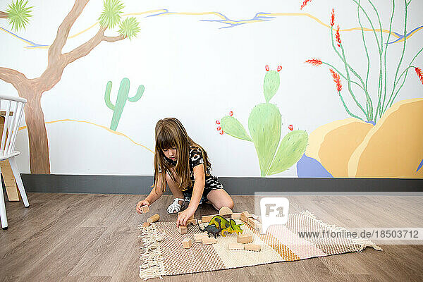Little girl plays on the ground with blocks and dinosaurs