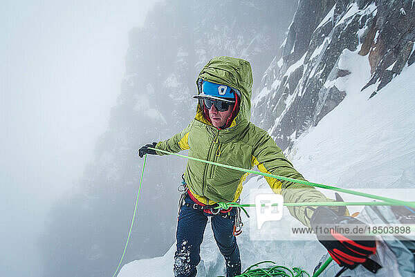 Ice climber belaying while climbing in winter