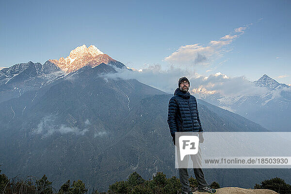A man looks out over the Himalayas with sunset light on a mountain.