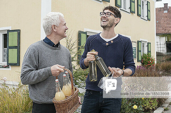 Father and son holding bottles of white wine and apple juices and laughing  Bavaria  Germany