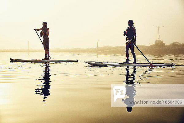 two friends standup paddle boarding on a foggy morning at sunrise