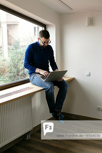 man in blue sweater and jeans is working alone at home with laptop