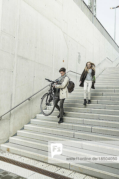Young man carrying a bicycle and teenage girl holding skateboard moving down the stairs  Munich  Bavaria  Germany
