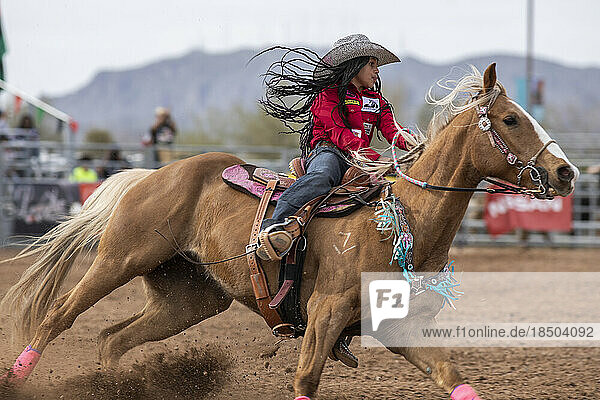A young woman rides in the barrel racing event at the AZ black rodeo
