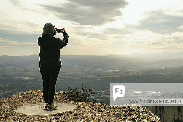 Unrecognizable girl taking a photo of a mountain landscape on top