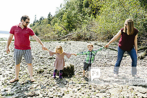 Straight on portrait of a family of four holding hands on a rocky beac