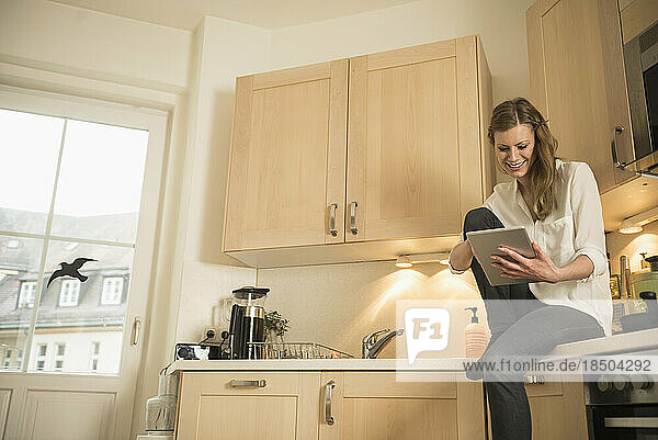 Young woman using digital tablet and sitting on kitchen worktop  Munich  Bavaria  Germany