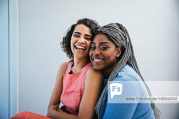 Portrait of cheerful lesbians sitting against wall at home
