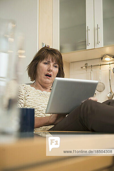 Senior woman looking shocked while using a digital tablet in the kitchen  Munich  Bavaria  Germany