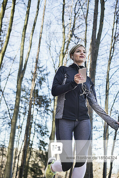 Young woman listening music on smart phone and jogging on fitness trail