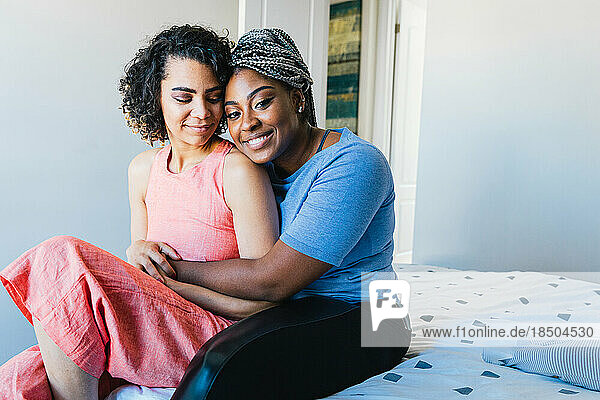 Portrait of cheerful woman embracing girlfriend while sitting on bed