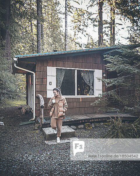 A woman is standing need a forest cabin with a cup of coffee