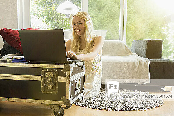 Beautiful young woman using laptop in the living room and smiling  Munich  Bavaria  Germany