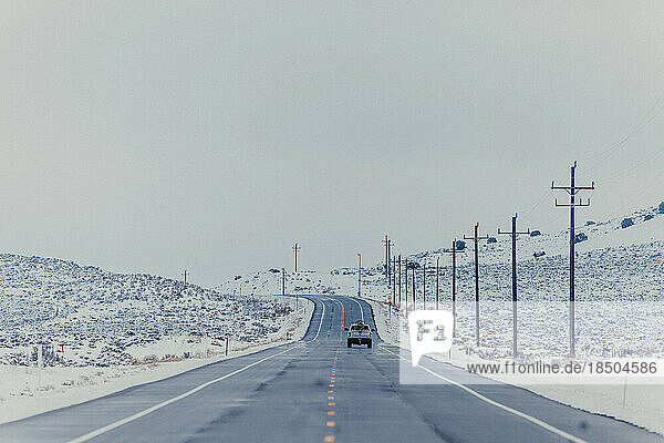 A truck travels down a long road in the winter.