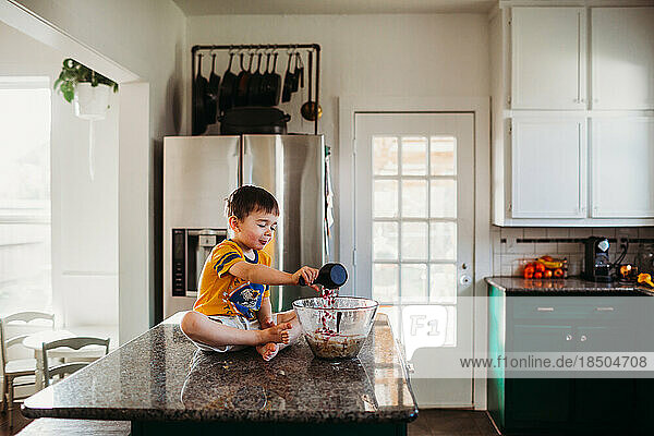Young boy pouring candy in to bowl on cookie batter in kitchen