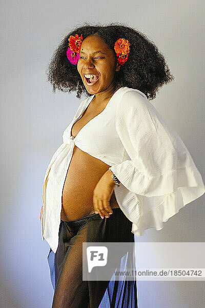A laughing pregnant woman stands proud with flowers in hair