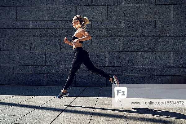 Woman in black sportswear training jumping outdoors in a sun light ray