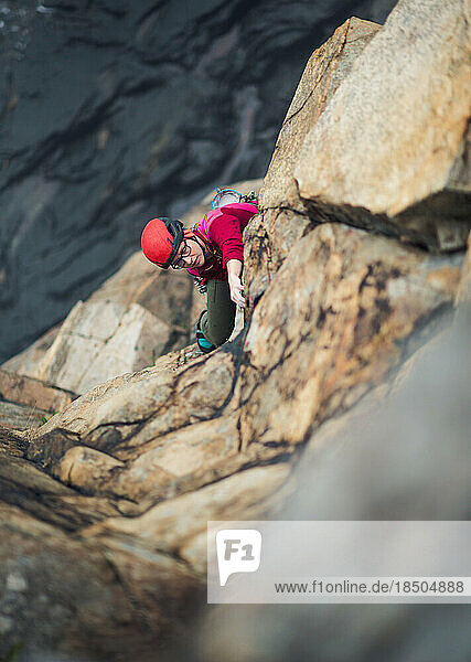 Woman wearing red trad climbing on lead with belayer below