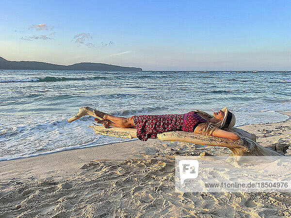 Woman in sundress lying on driftwood on beautiful white sand beach