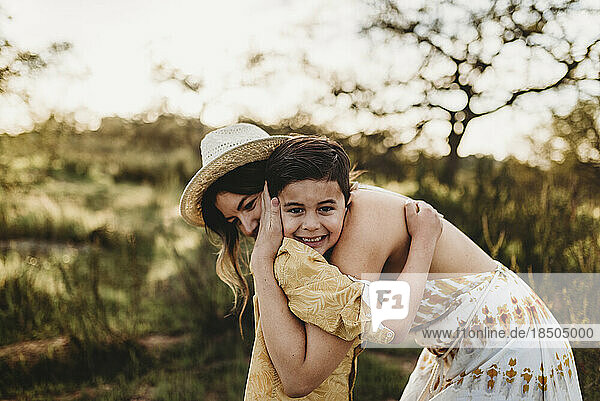 Side view of young mother and young son embracing and smiling in field