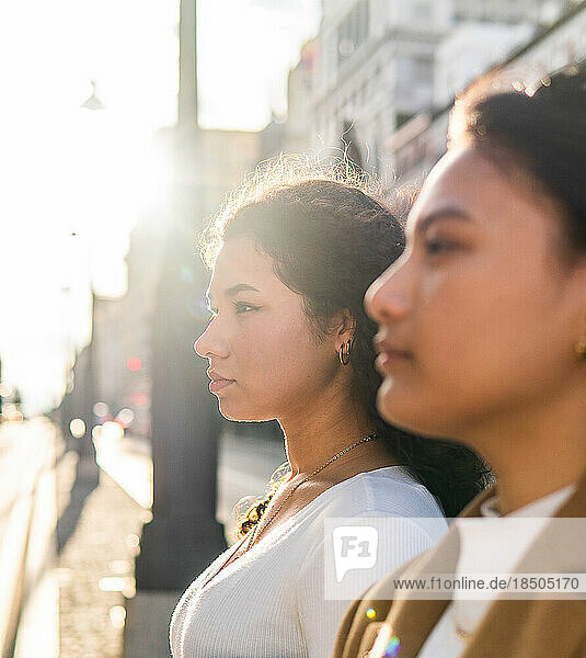 Stock photo of a profile shot of two friends standing looking away.