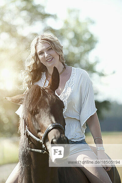 Portrait of a young woman riding a horse in farm and smiling  Bavaria  Germany