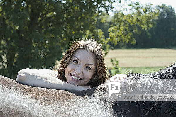 Portrait of a mature woman leaning on brown horse's back and smiling  Bavaria  Germany