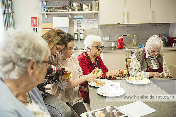 Senior women with girls peeling apple at rest home