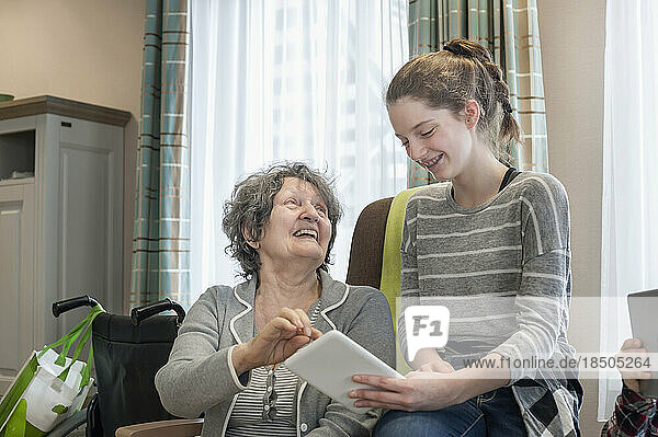 Senior women with granddaughter using digital tablet in rest home