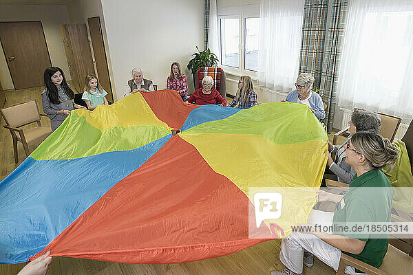 Girls with nurse and senior women doing gentle sports exercise with cloth in rest home