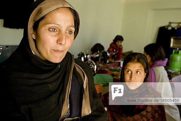 Afghan businesswoman gazes thoughtfully away from her workroom where seamstresses produce garments and curtains.